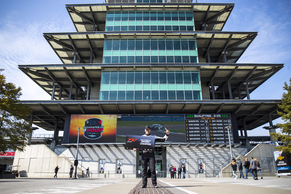 James Clay holding Driver's Champion sign in front of Indy building